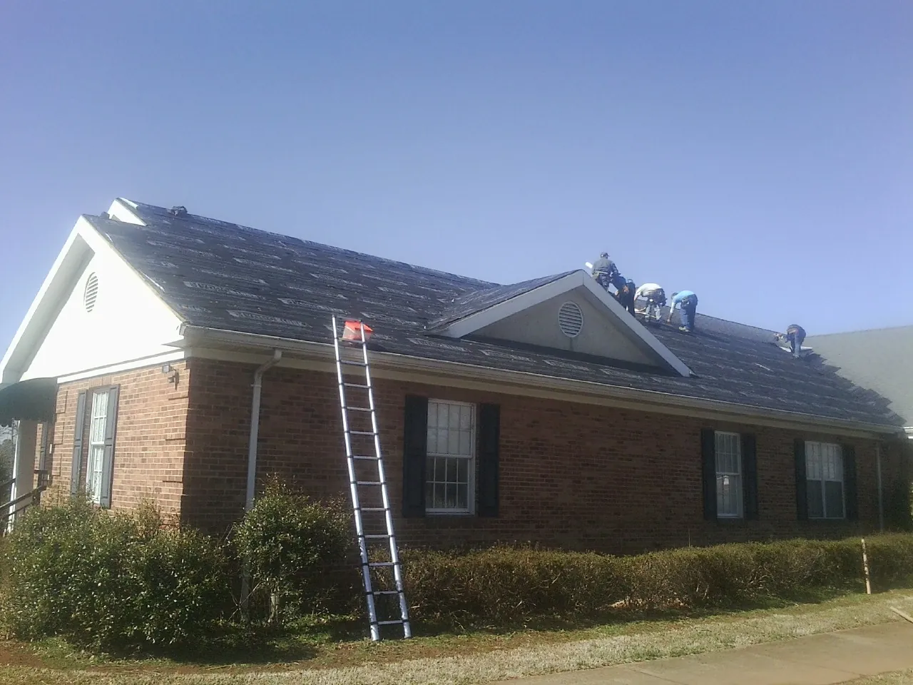 Crew tearing shingles off a brick ranch roof with a ladder set — Emergency Roof Repair work by our crew in South Saint Paul
