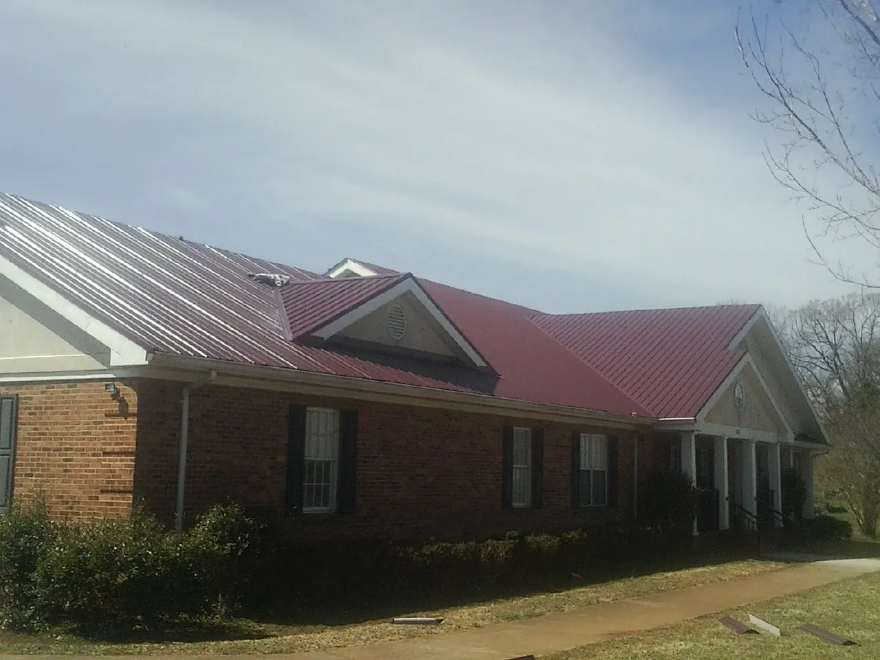 Red metal roof with gabled entries on a long brick building, from a Hail Damage Roof Repair job in South Saint Paul