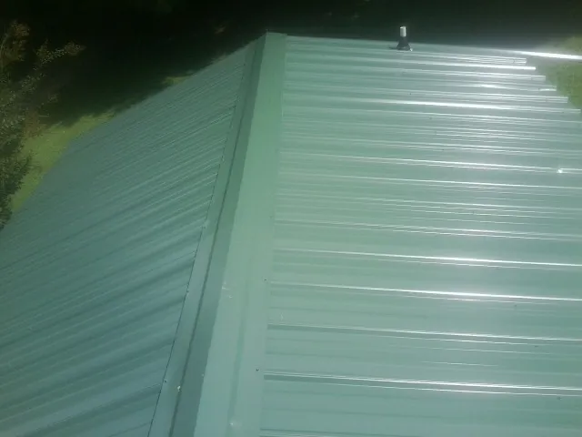 New green metal panels meeting at the ridge of a roof — Flat Roof Repair work by our crew in South Saint Paul
