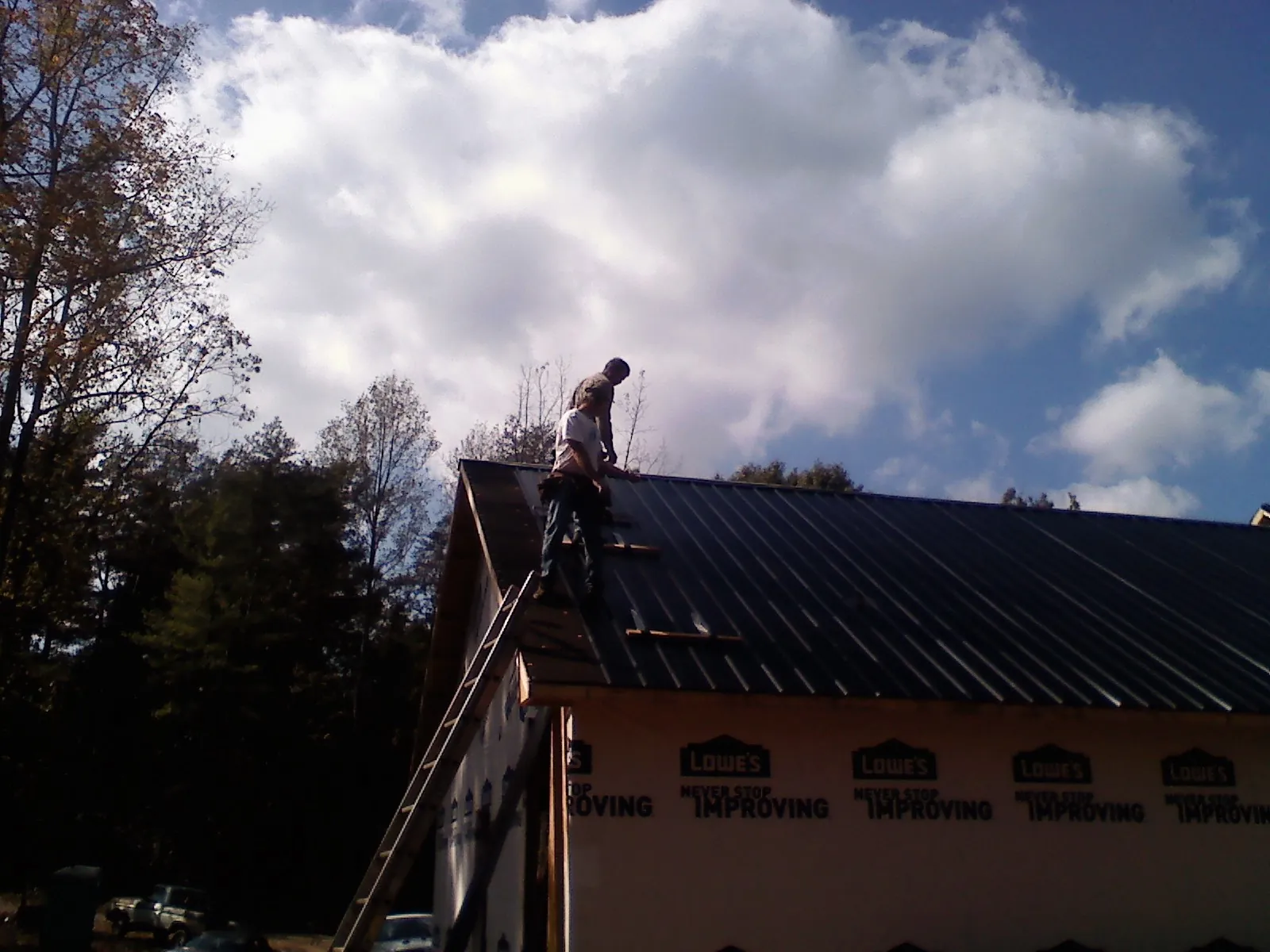 Roofer fastening dark metal panels high against a cloudy sky, from a Roof Inspection job in South Saint Paul