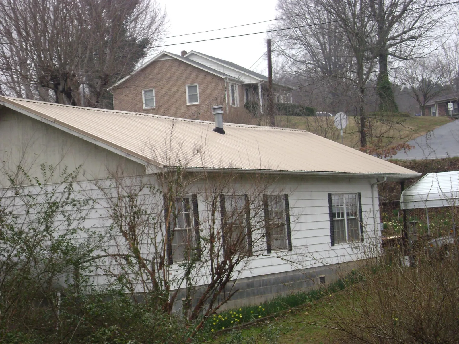 Tan metal roof on a white sided house set into a hillside — Commercial Roofing by Roofing Brothers in South Saint Paul